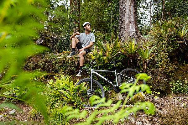 Mountainbiker ruht im grünen Wald neben dem Rad.