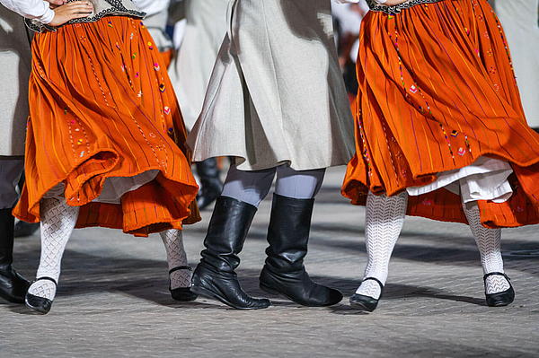 Nahaufnahme von Beinen beim lettischen Volkstanz orangefarbene Trachtenröcke Stiefel und Strumpfwaren