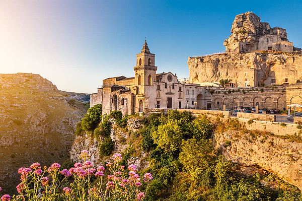 Historische Altstadt von Matera mit Kirche und Felsen im Abendlicht.