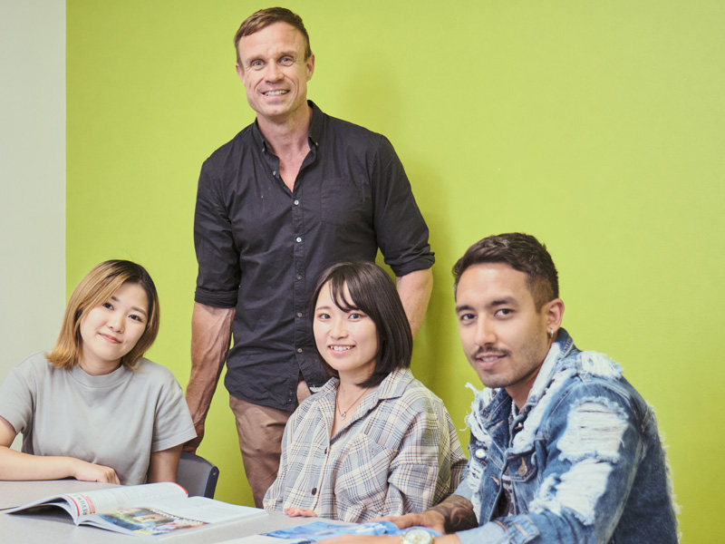 Englischlehrer mit drei Lernenden im Klassenzimmer der Langports Brisbane vor grüner Wand