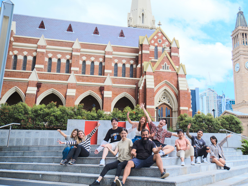 Gruppe von Sprachschülerinnen und Sprachschülern entspannt auf den Treppen vor der Kirche in Brisbane