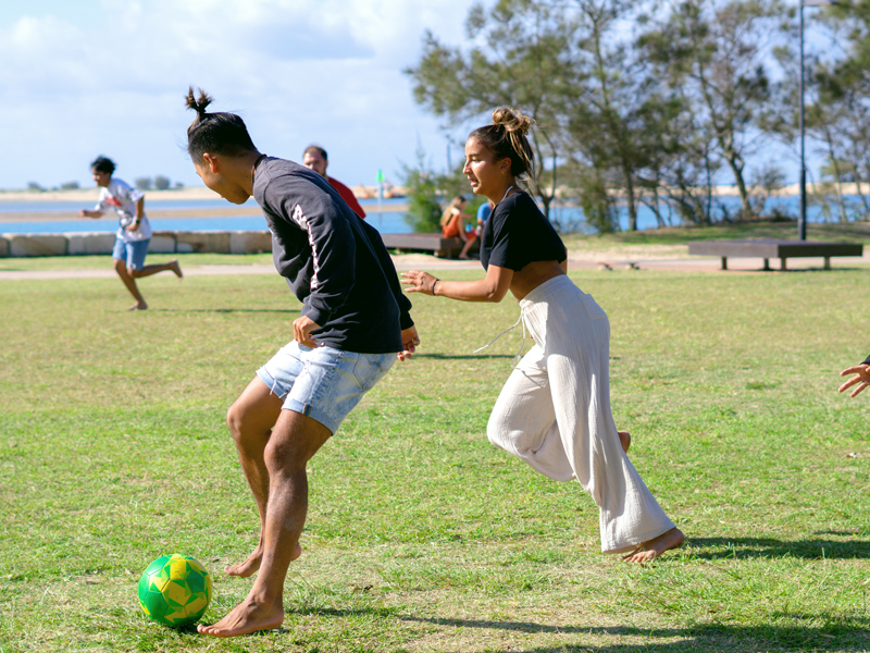 Sprachreisende spielen Fußball am Strand und üben Englisch im Team