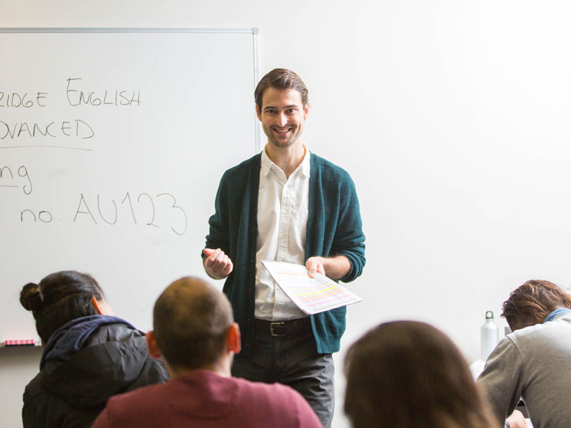 Lehrkraft führt Unterricht an der Tafel durch und erklärt Inhalte eines Cambridge-English-Kurses