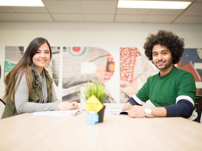 Zwei Teilnehmende arbeiten gemeinsam im Klassenraum mit moderner Wandgestaltung