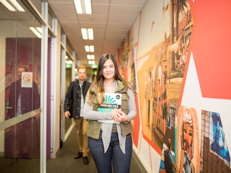 Sprachschülerin hält Lehrbuch und steht im bunt gestalteten Flur der Discover English Schule