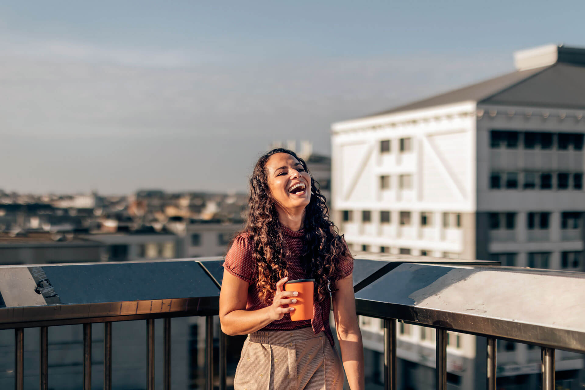 Teilnehmerin einer Sprachreise genießt eine Pause auf einer Dachterrasse und blickt lachend über die Stadt während ihres Sprachaufenthalts im Ausland.