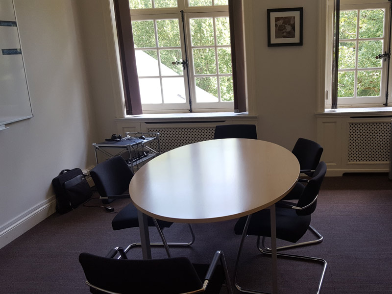 Kleiner Unterrichtsraum mit ovalem Tisch und Tageslicht durch große Fenster