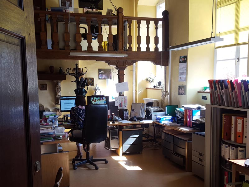 Büro der Sprachschule mit Schreibtischen, Aktenordnern und einer Mitarbeiterin bei der Arbeit