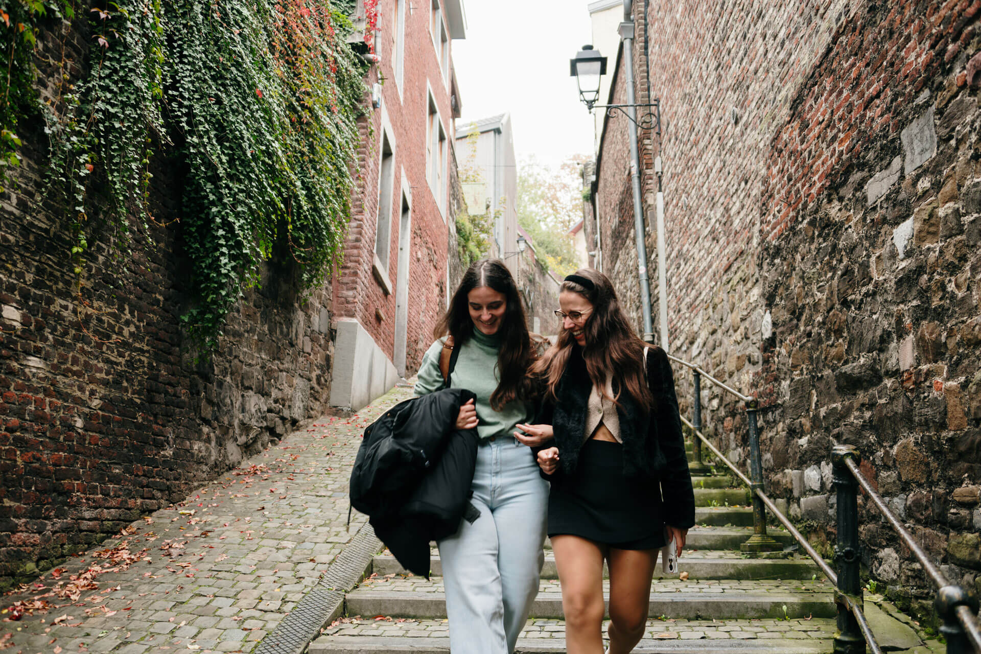 Zwei Freundinnen spazieren lachend durch eine schmale Gasse in der Altstadt von Lüttich