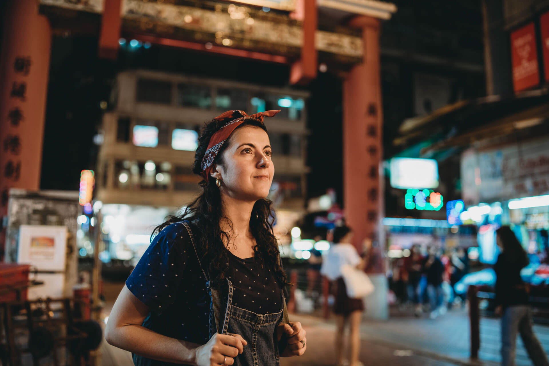 Person spaziert am Abend durch ein belebtes Stadtviertel in China mit leuchtenden Schildern und traditionellem Torbogen