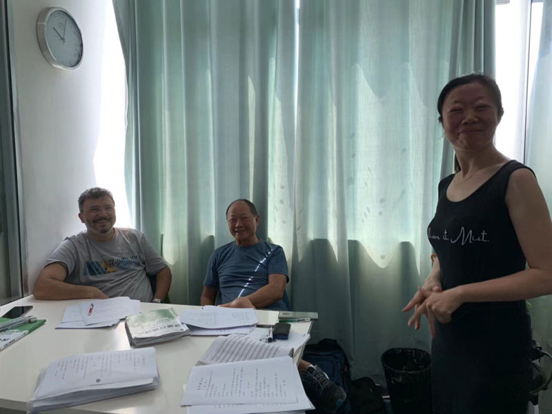 Kleine Gruppe im Chinesischunterricht mit Lehrkraft vor hellgrünem Vorhang