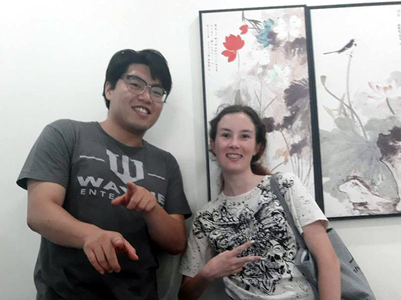 Zwei Personen posieren lächelnd vor traditionellem chinesischen Wandbild in der Sprachschule