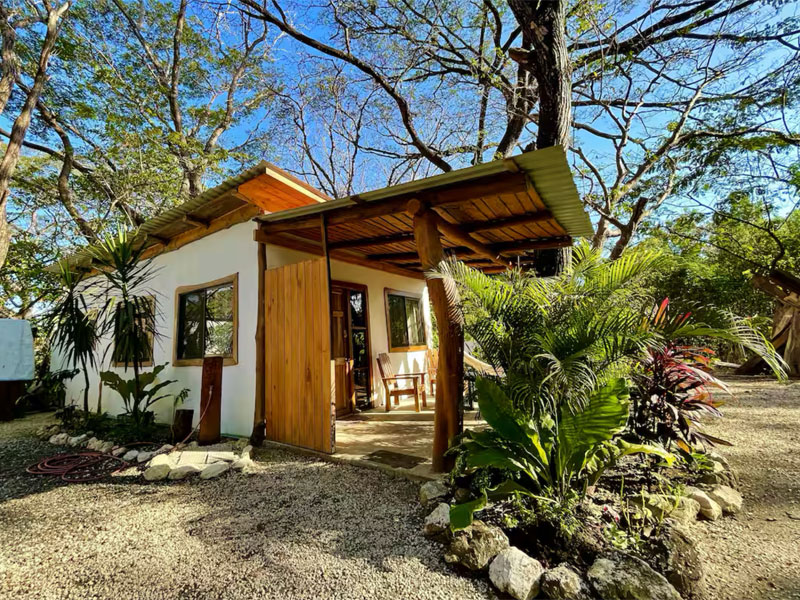 Iona Studio in Sámara mit überdachter Veranda, Holzelementen und tropischen Pflanzen im Gartenbereich.