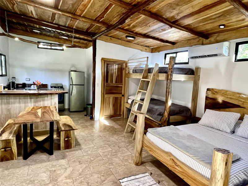 Offenes Studio-Apartment in Sámara mit Holzbett, Etagenbett, Essbereich und voll ausgestatteter Küche im rustikalen Design.