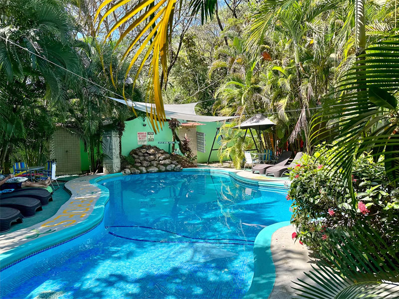 Tropischer Pool der Villas Verdes in Sámara, umgeben von Palmen, Liegestühlen und schattigen Ruhebereichen.