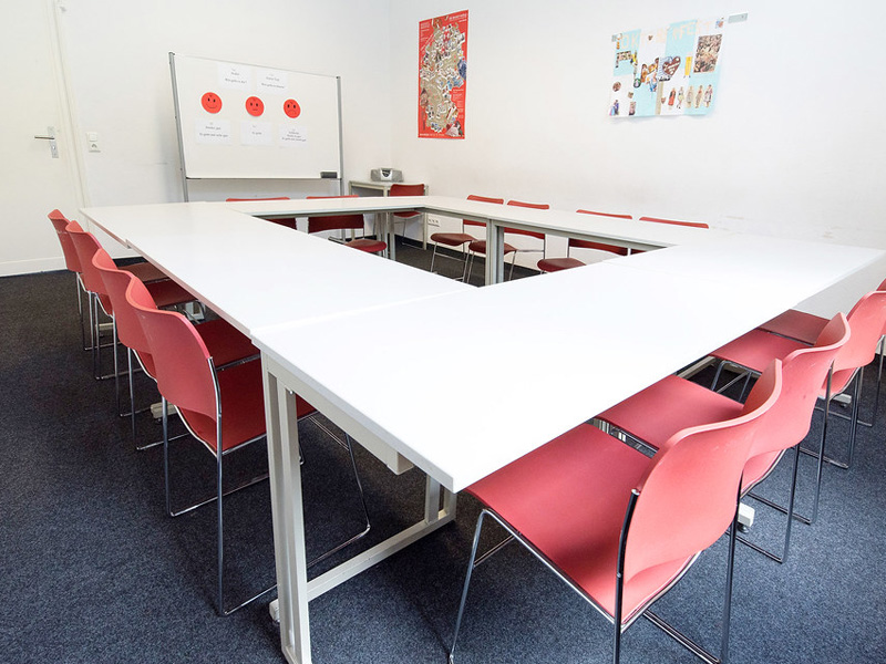 Heller Klassenraum mit moderner U-förmiger Tischanordnung und roten Stühlen