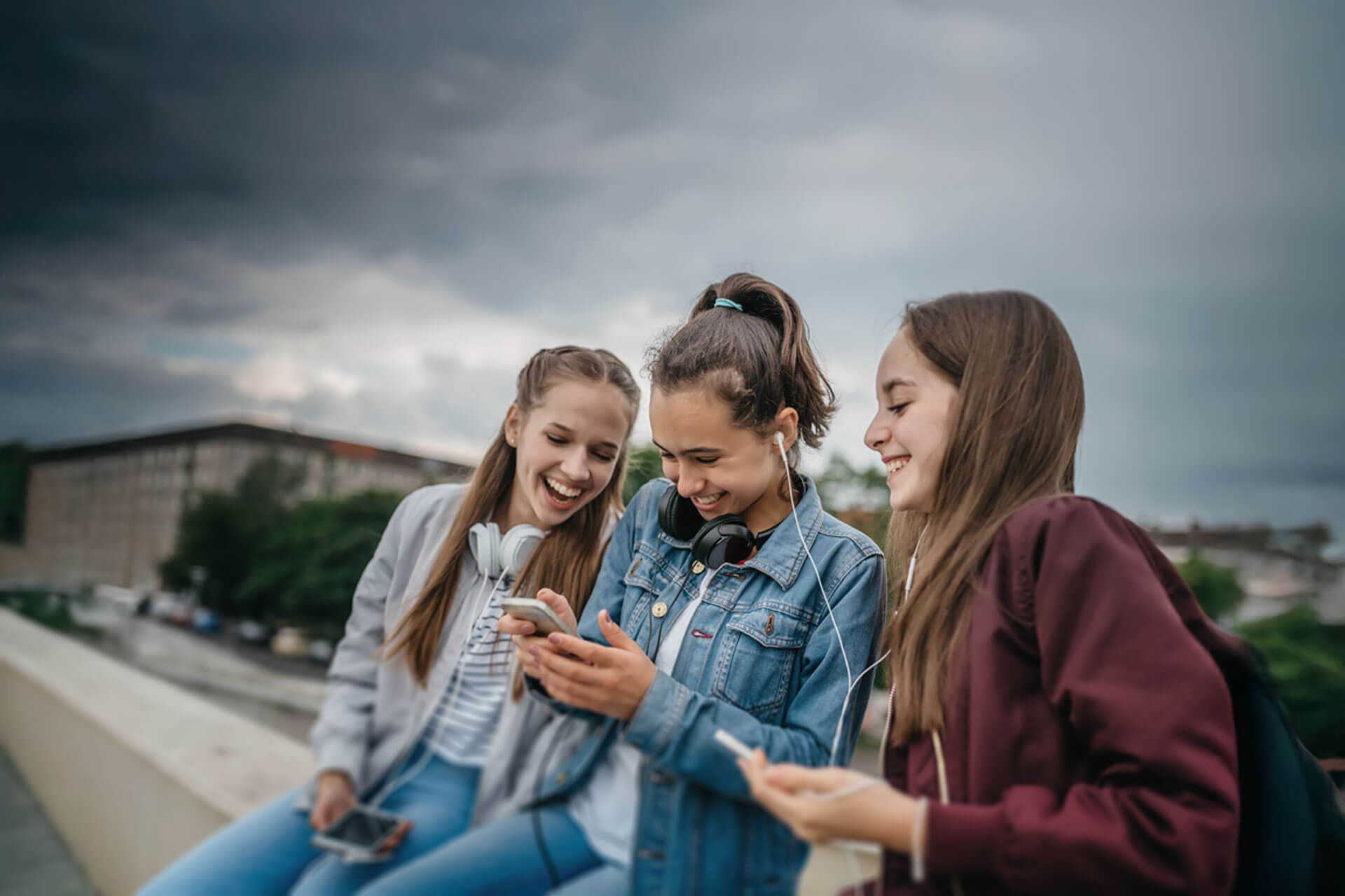Drei Jugendliche sitzen im Freien und lachen gemeinsam über Inhalte auf dem Smartphone