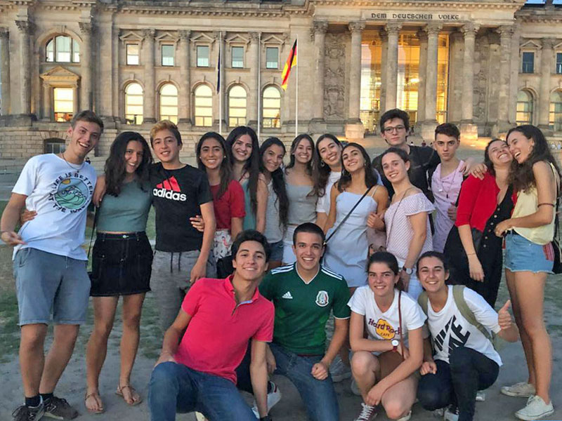 Gruppe junger Sprachreisender vor dem Reichstagsgebäude während eines kulturellen Ausflugs in Berlin.