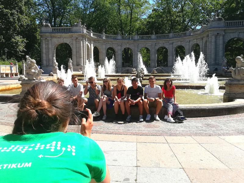 Sprachreisegruppe sitzt für ein Erinnerungsfoto an einem Brunnen in Berlin während eines Ausflugs nach dem Deutschkurs.