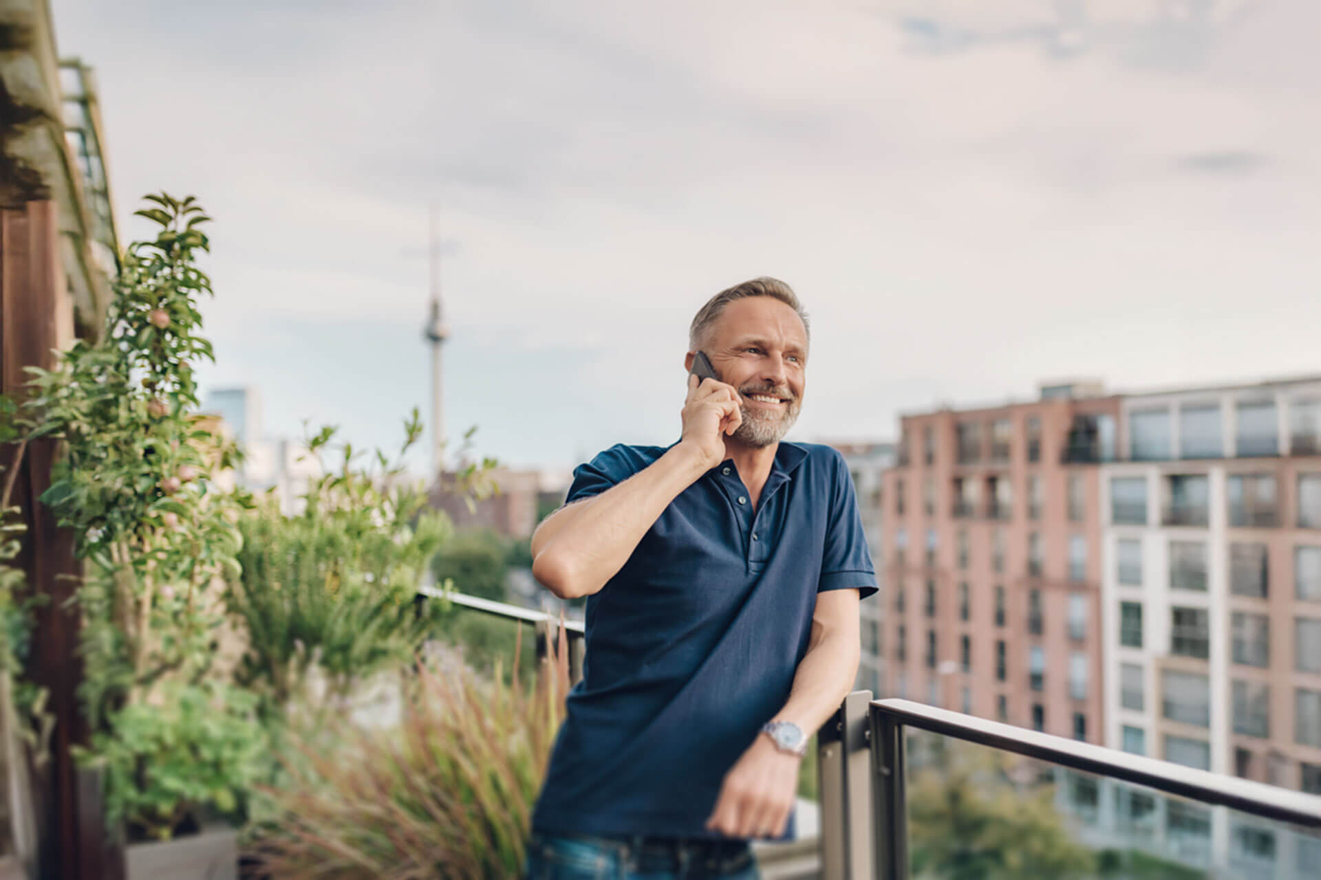 Mann telefoniert entspannt auf einer Berliner Dachterrasse mit Blick auf die Stadt