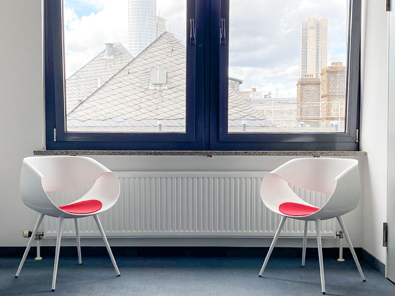 Sitzecke mit zwei modernen Stühlen und Fensterblick auf Frankfurter Skyline