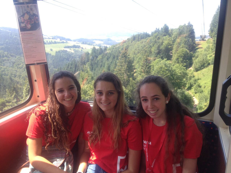 Drei Schülerinnen in roten T-Shirts sitzen in einer Seilbahn mit Blick auf den Schwarzwald