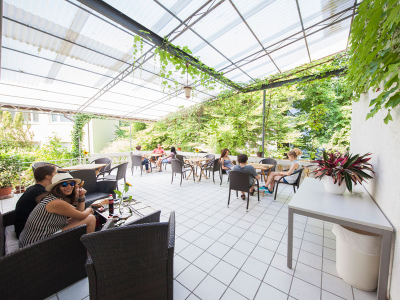 Überdachte Terrasse mit Sitzgelegenheiten und grüner Umgebung an der Alpadia Sprachschule Freiburg