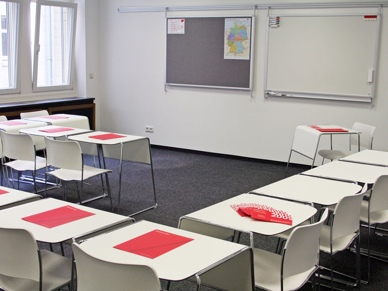 Klassenzimmer mit weißen Tischen und roten Mappen