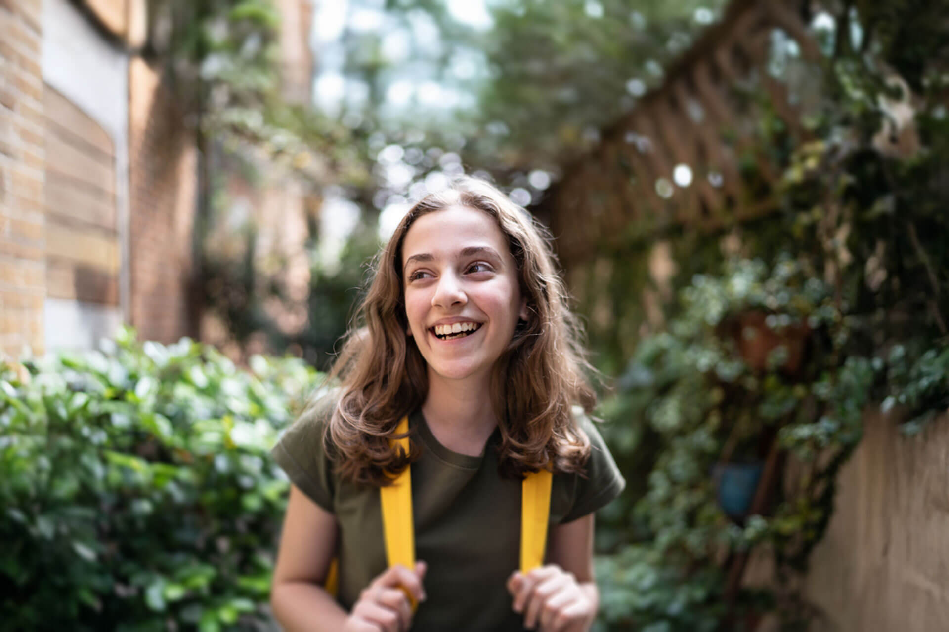 Lachende Jugendliche mit gelbem Rucksack steht im begrünten Innenhof in Heidelberg