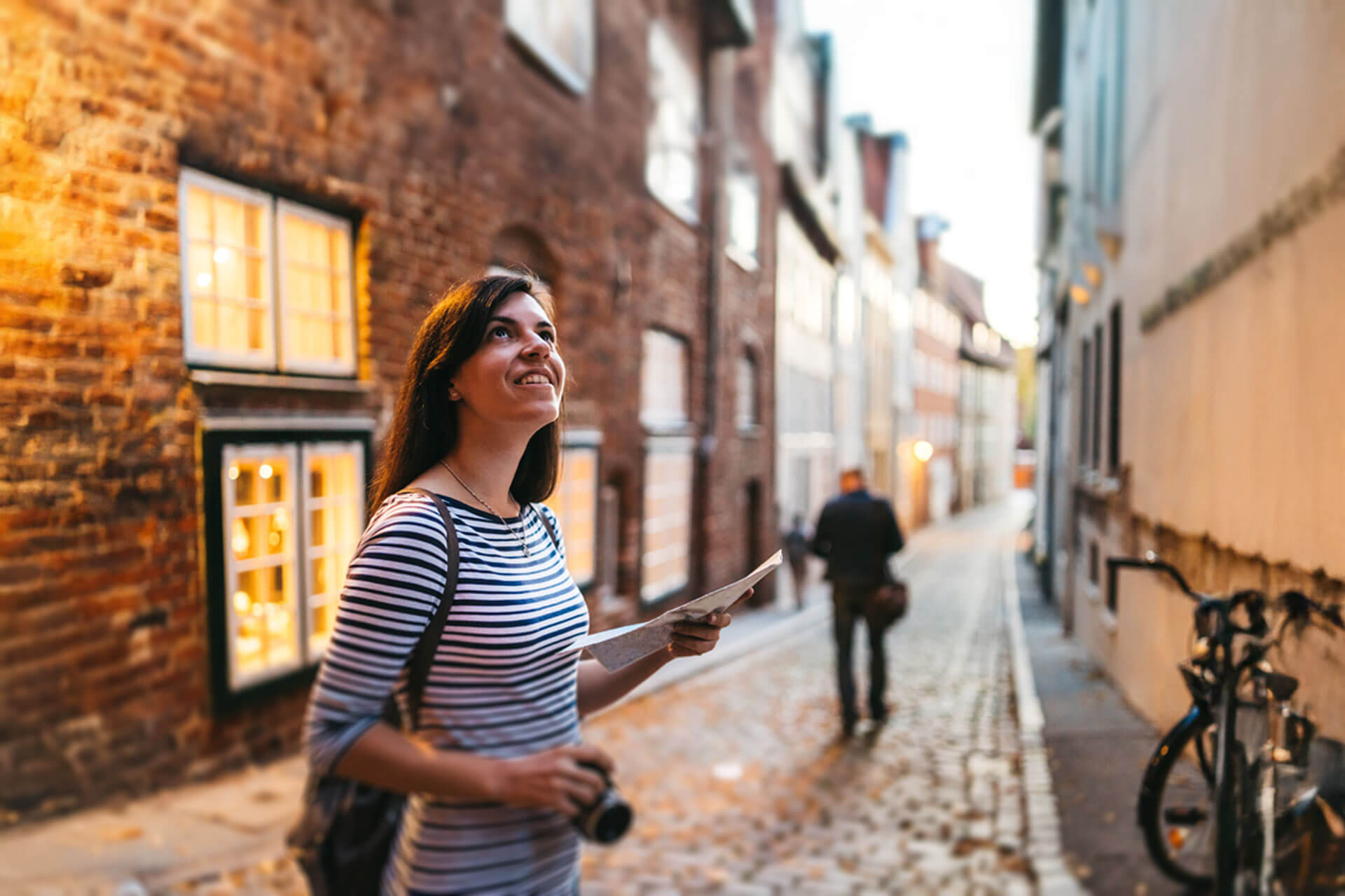 Person mit Stadtplan und Kamera erkundet eine historische Altstadtgasse in Heidelberg bei warmem Abendlicht