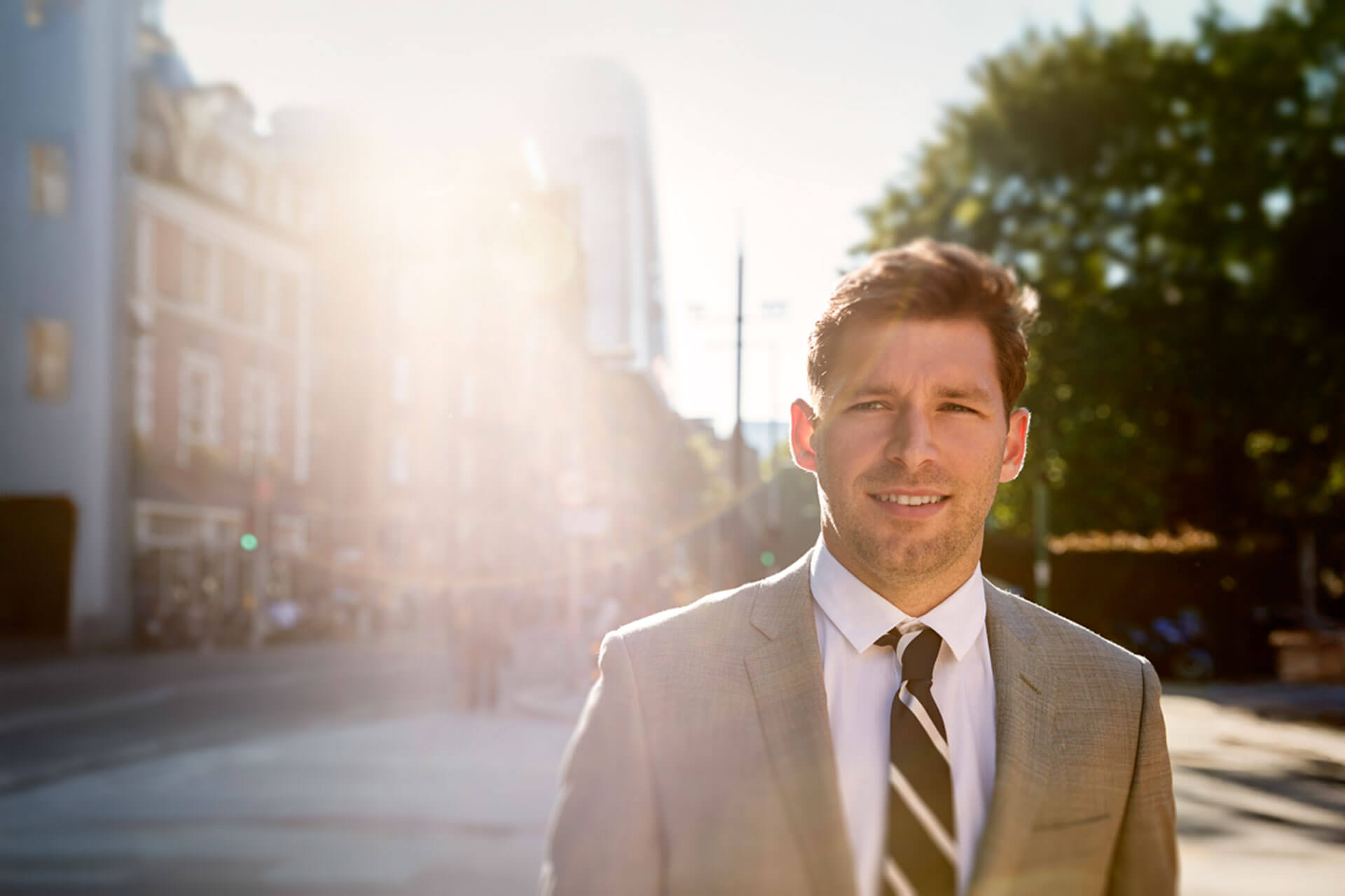 Person im Anzug steht in der Sonne auf einer Straße in Heidelberg und blickt freundlich in die Kamera