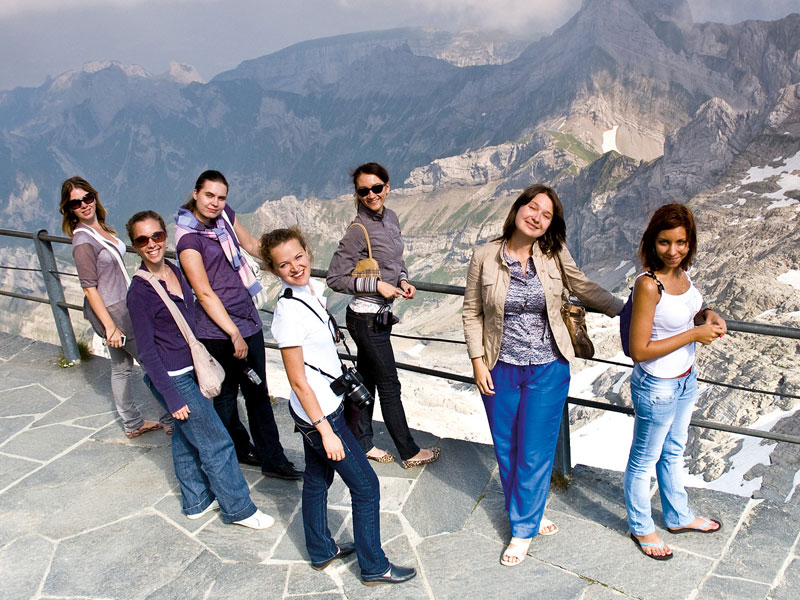 Gruppe von Sprachlernenden genießt den Ausblick auf die umliegenden Alpen während eines Ausflugs