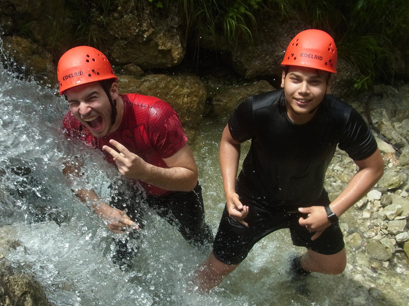 Zwei Jugendliche mit Helmen stehen lachend in einem Gebirgsbach während einer Canyoning-Tour