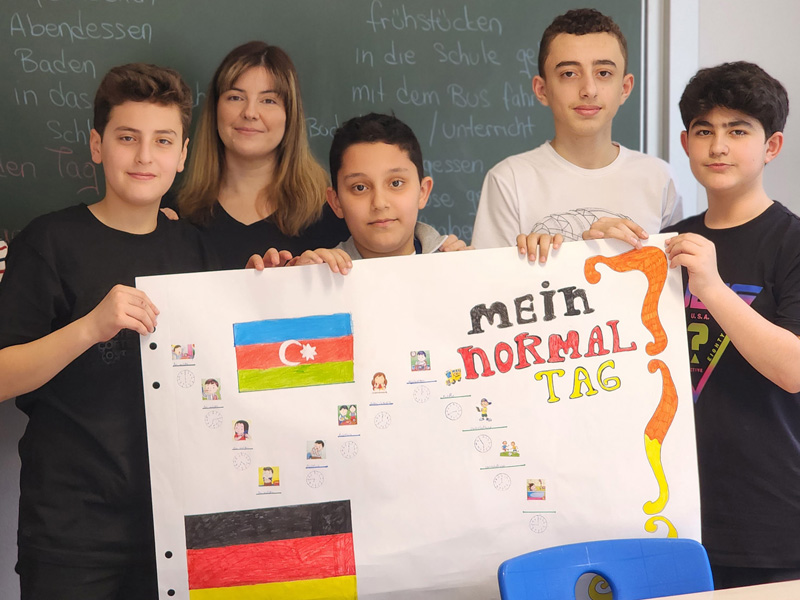 Gruppe Jugendlicher präsentiert im Klassenraum ein bunt gestaltetes Plakat zum Thema „Mein normaler Tag“