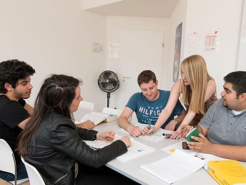 Kleine Lerngruppe arbeitet gemeinsam mit Lehrkraft an Sprachübungen am Tisch