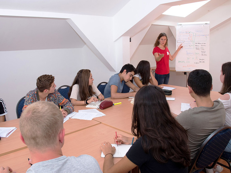 Jugendliche nehmen am Unterricht teil, während die Lehrkraft Inhalte an einem Flipchart erklärt