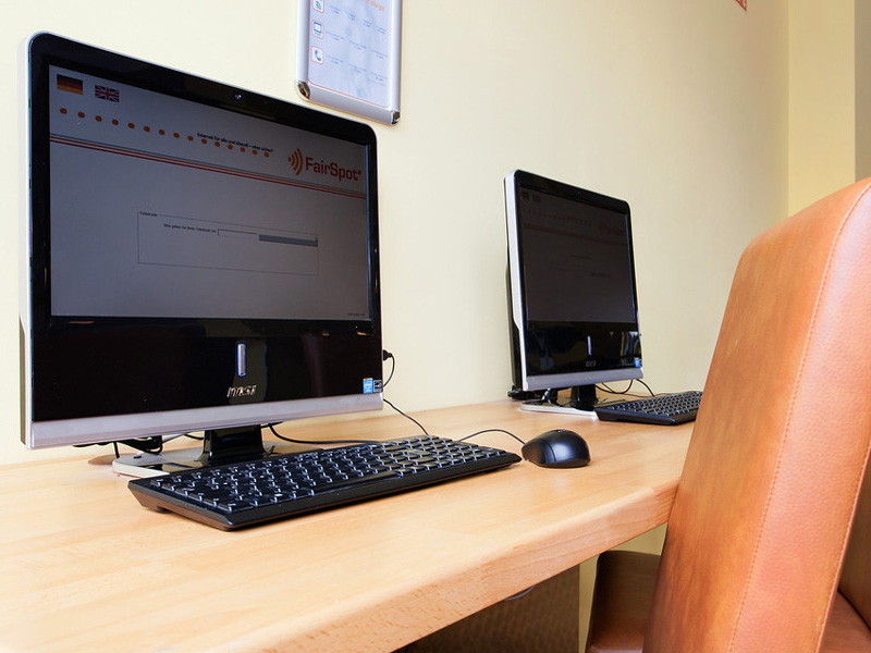 Computerarbeitsplätze mit modernen Monitoren und Ledersesseln im Lernbereich der Sprachschule