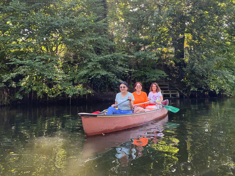 Drei Personen paddeln gemeinsam in einem Kanu auf einem ruhigen Fluss in Münster