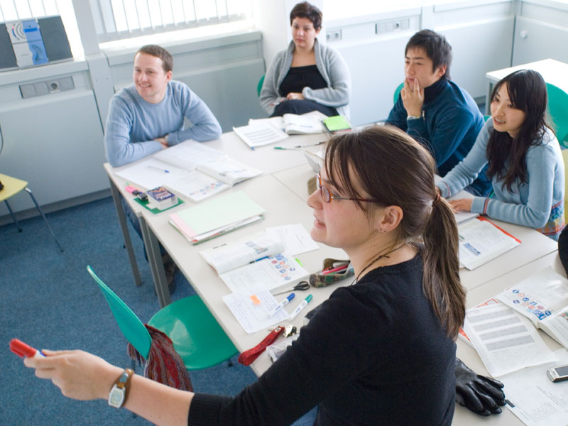 Lehrkraft erklärt Grammatikregeln an der Tafel, während die Gruppe aufmerksam folgt