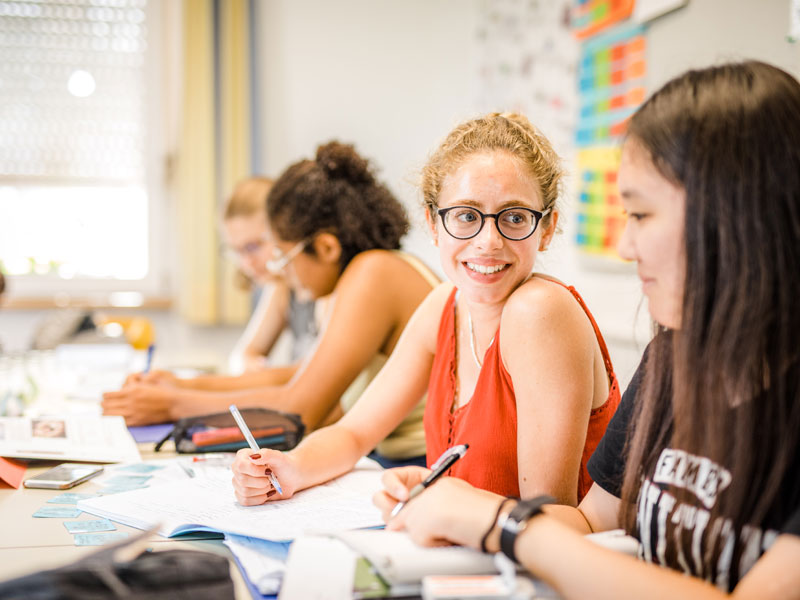 Zwei Schülerinnen arbeiten gemeinsam im Unterricht und lächeln sich an