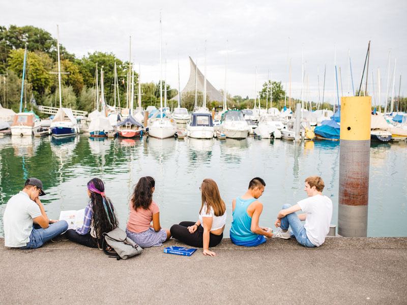 Gruppe Jugendlicher sitzt am Hafen von Radolfzell mit Blick auf Segelboote