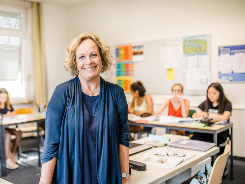 Lehrkraft steht vor einer kleinen Lerngruppe im hellen Klassenraum