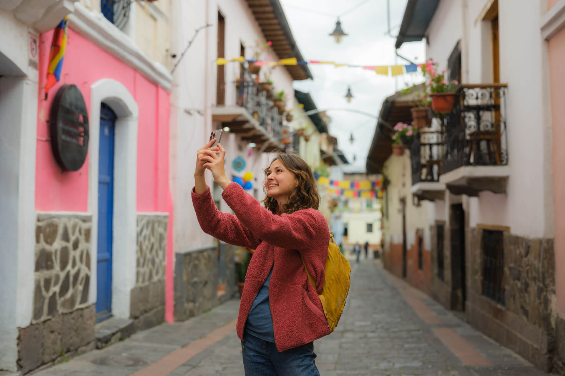 Person macht ein Selfie in einer bunten Gasse von Quito mit typischer kolonialer Architektur und farbenfrohen Fassaden