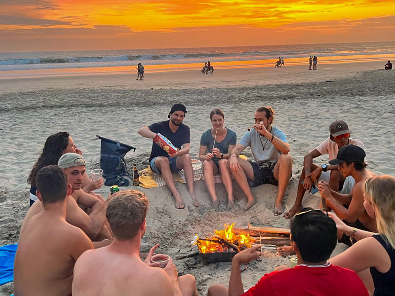 Spanischlernende sitzen gemeinsam am Lagerfeuer am Strand von Montañita bei Sonnenuntergang
