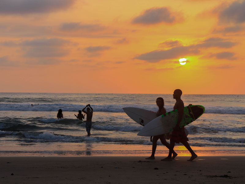 Zwei Surfer mit Boards laufen am Strand von Montañita in der Abendsonne entlang