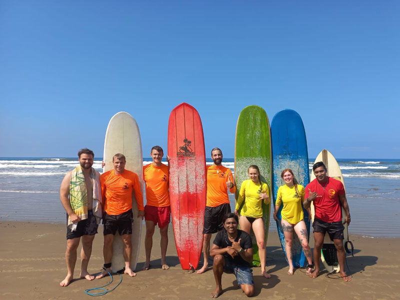 Surfgruppe der Montañita Spanish School posiert mit bunten Brettern am Strand