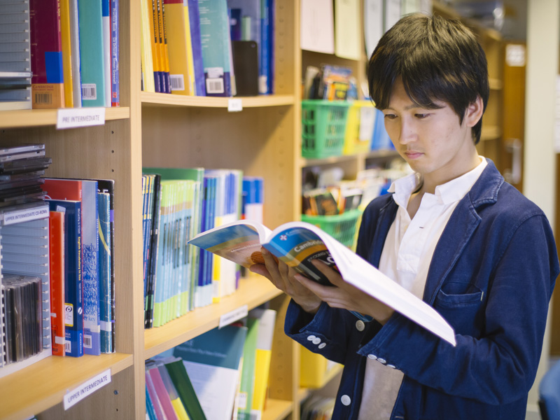 Student liest konzentriert in einem Lehrbuch in der Schulbibliothek