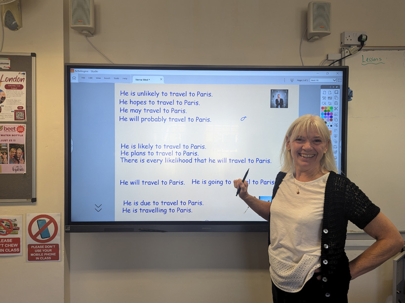 Lehrerin steht vor einem digitalen Whiteboard und erklärt englische Satzstrukturen