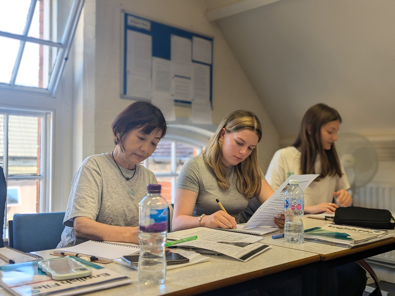 Drei Personen arbeiten konzentriert im Unterricht an Grammatik- und Lesetexten