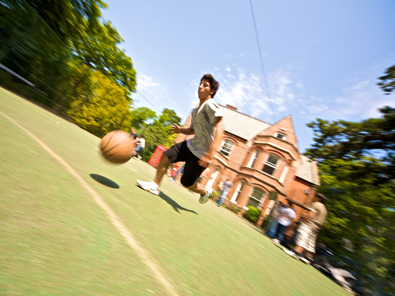 Schüler spielt Basketball auf dem Sportplatz der Kings Sprachschule Bournemouth bei Sonnenschein.